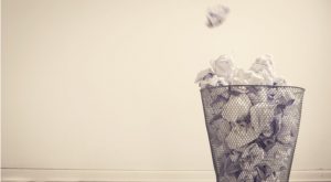 Image of paper being thrown into a trash can with a sand-colored background