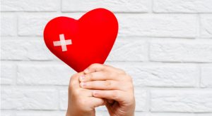 Image of hands holding a red heart with a patch on it and a background comprised of white bricks