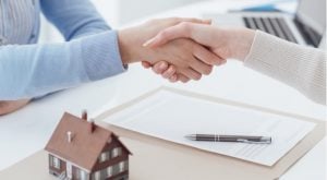 two people shaking hands over a desk with mortgage papers and a small model of a house