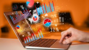 best investments: a hand using the touchpad on a laptop. a concept image of figures and charts is emerging from the laptop screen.