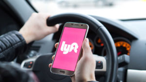 A Lyft (LYFT) driver holds a smartphone displaying the pink Lyft logo in the car.