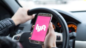 A Lyft (LYFT) drive holds a smartphone showing the pink Lyft logo while in the car.