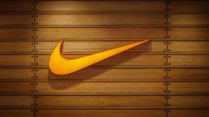 The swoosh logo for Nike Inc (NKE) is displayed on a wall made of wood panels.