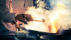 A person cooks something in a smoking wok
