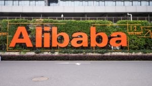 The Alibaba (BABA) logo featured on the exterior of an office building with bushes in the background