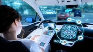 A young woman reads a book while behind the wheel of a self-driving car.