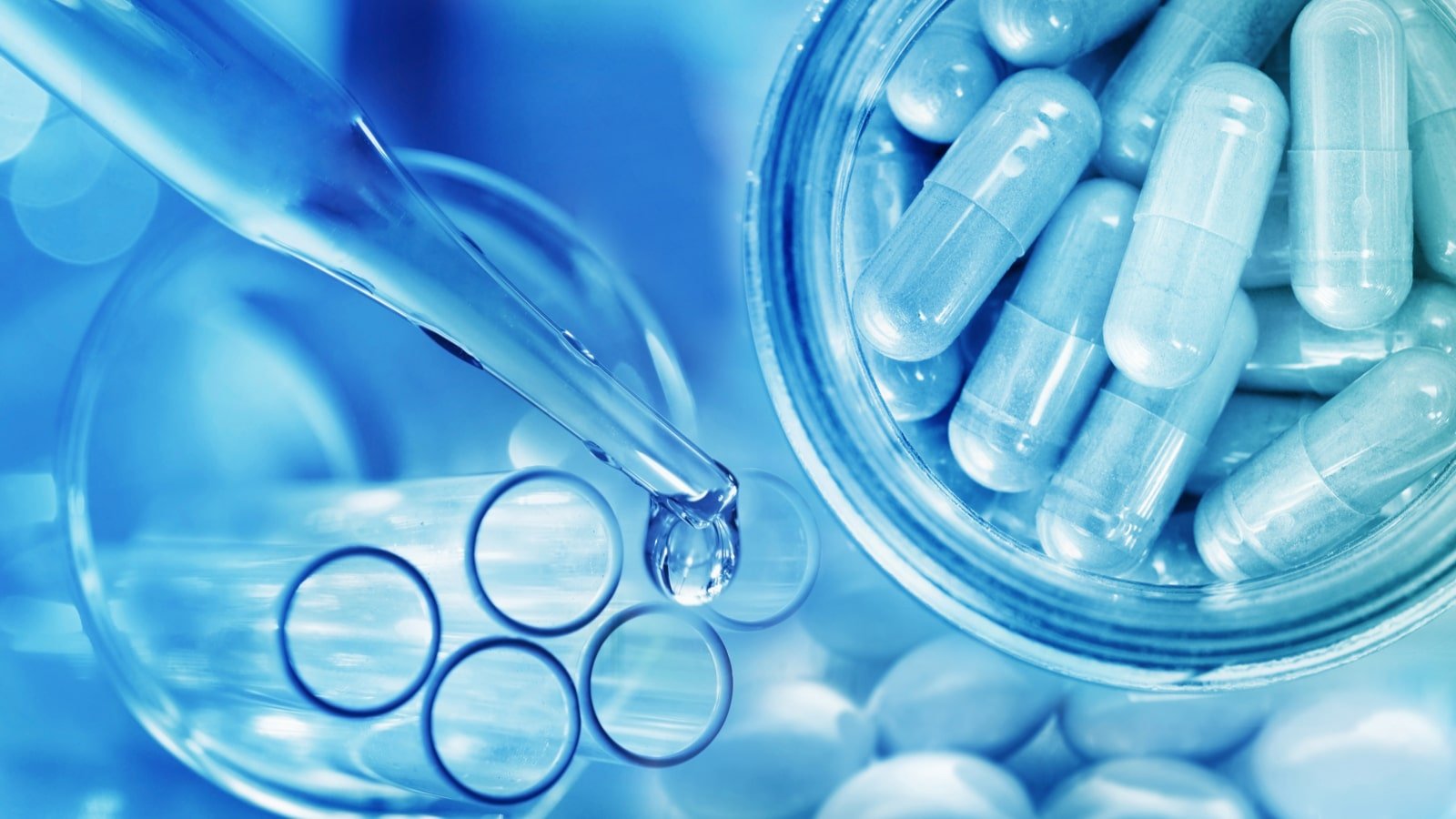 a number of test tubes and capsules are pictured under a cool blue light representing biotech stocks