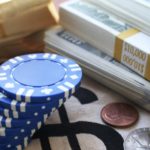 Blue poker chips stacked next to three stacks of $100 bills representing blue chip stocks. undervalued blue-chip stocks