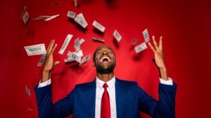 Man in blue formal wear tuxedo standing as money 'rains' on him, isolated on red vivid background.