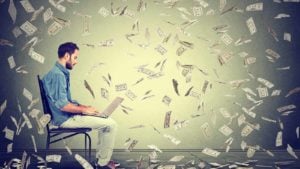 a man sitting on a chair, typing on a laptop while cash falls from the ceiling