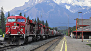 A photo of a large red train with a CP logo at a train station with mountains in the background.