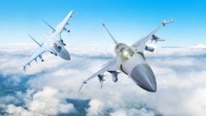 A photograph of two jet fighters flying above clouds. defense stocks