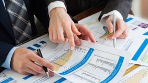 Two businessmen holding and pointing at earnings charts.