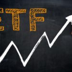 A person drawing a line graph with the phrase "ETF" in large letters on a chalkboard. index funds to buy
