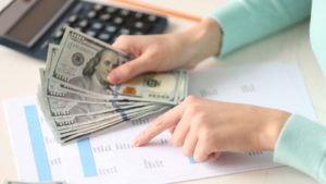 A photo of a person holding money while reading statistics on a page.