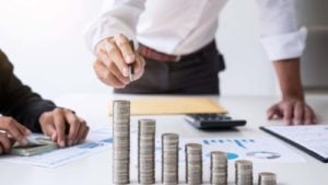 two businesspeople sit at a table stacking up coins in the shape of an ascending bar chart