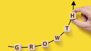 Wooden blocks spelling out "growth" form a steep upward arrow on a bright yellow background.