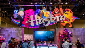 The Hasbro (HAS) logo with several of the brand's characters behind it is on display in a convention hall.