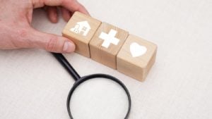 A close-up shot of a hand choosing wooden blocks with emoticons related to health insurance.