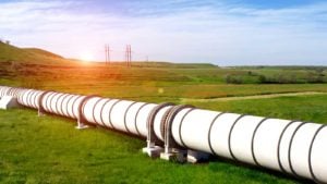 Natural gas pipeline through green field with blue sky above