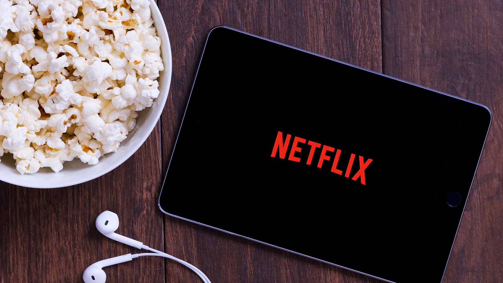 The Netflix (NFLX) logo on a tablet with earbuds and a nearby bowl of popcorn.