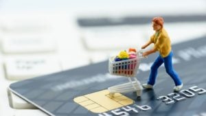 a figure of a shopper standing on top of a credit card. best retail stocks to buy in April