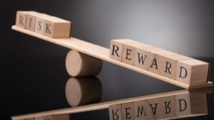 Two sets of blocks with the words "risk" and "reward" are placed on a seesaw with "reward" tipping downward.