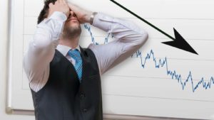 a frustrated man with a white board behind him that features a black downward arrow