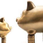 small pig figurine on top of short stack of coins next to large pig figurine on top of large stack of coins. represents small-cap stocks to buy