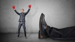 a tiny man with boxing gloves standing next to the feet of a giant man whom he presumably knocked out