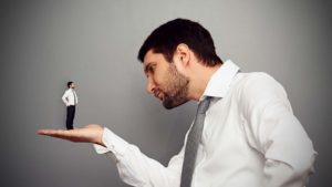 image of a large business man looking at a small businessman standing in the palm of his hand