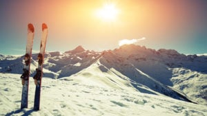 Skis basking in the sun atop a snow-covered mountain.