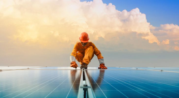 worker standing on solar panels with clouds and blue sky as backdrop