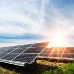 Solar panels in an open area, with the sun shining over them; solar stocks to buy now