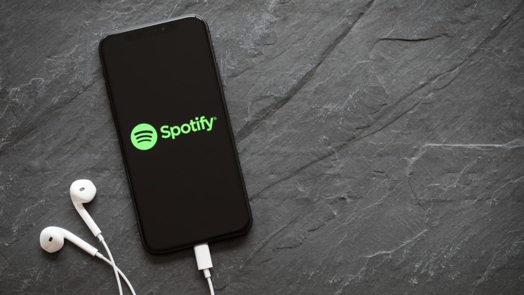 Spotify (SPOT) logo is on the screen of a smartphone with headphones plugged in.