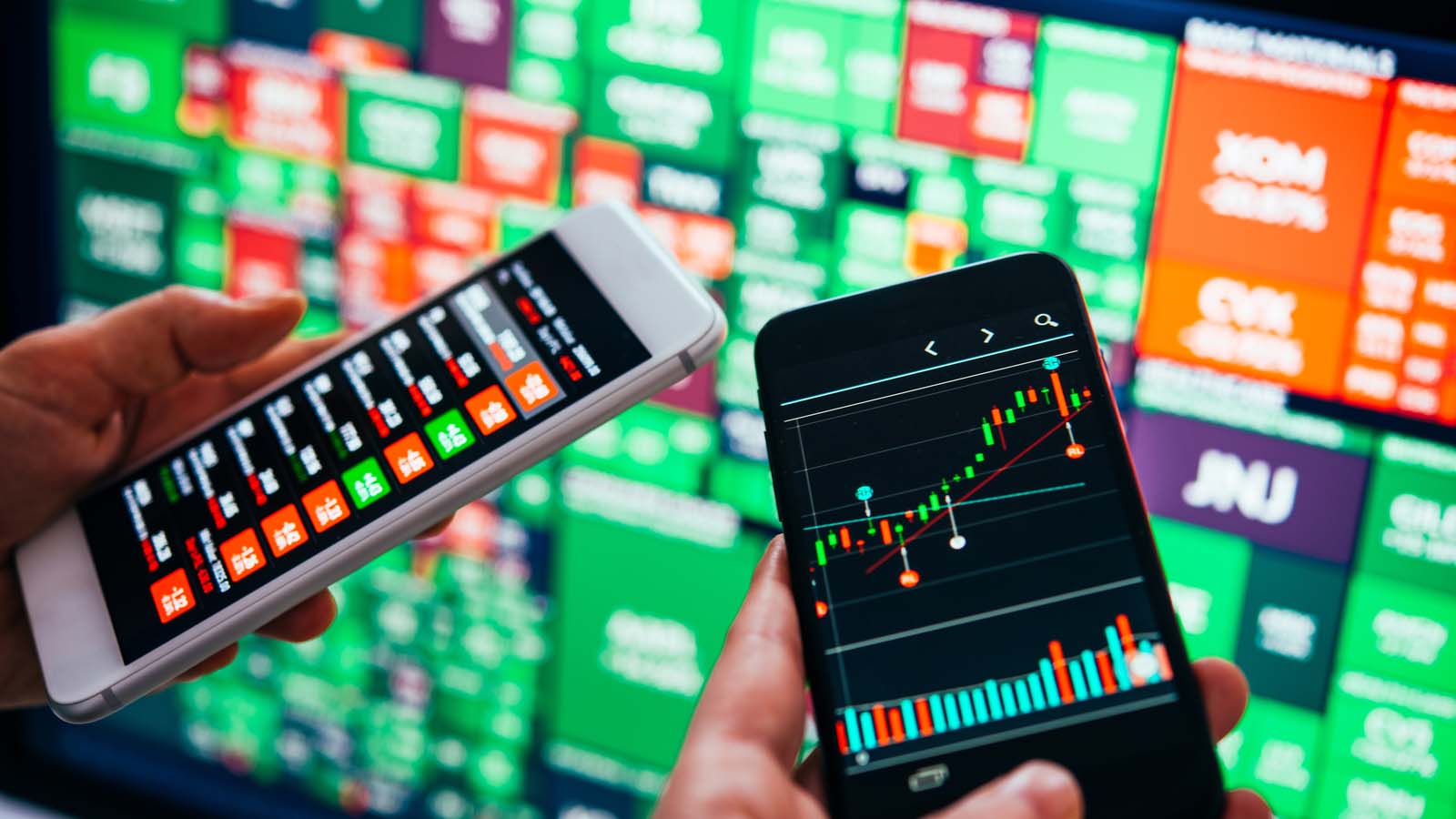 Low-beta stocks: traders use smartphones to trade stocks in front of a wall of green and red tickers