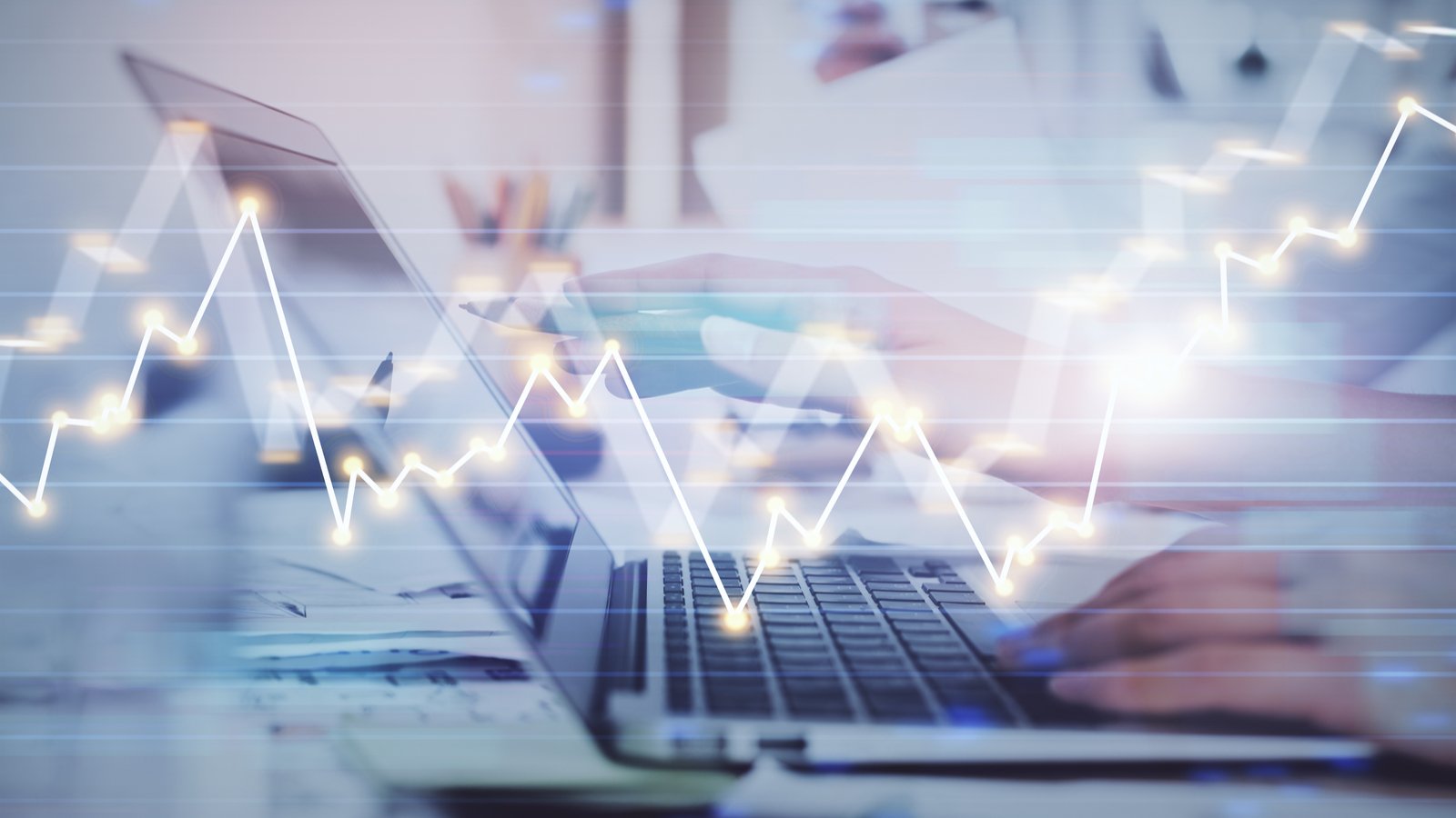 A graphic of a person's hands resting on a laptop with a stock line graph moving through it