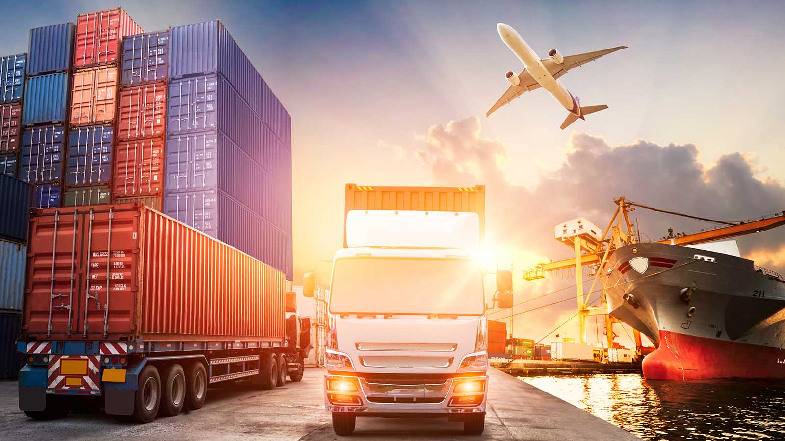 A cargo ship, containers, truck, and cargo plane in front of a sunny sky.