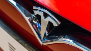 A close-up of the Tesla (TSLA stock) logo on the hood of a red Tesla car.