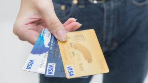 An outstretched hand holds three different Visa credit cards. stocks to buy