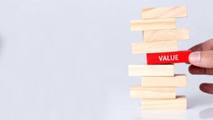 A hand pulls a red block with the word "Value" on it out of a Jenga set.