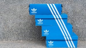 An image of four blue and white Adidas Originals shoe boxes stacked on top of each other with the three white stripes on each box lined up with each other in front of a speckled stone wall.