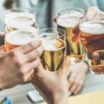 photo of peoples' hands clinking glasses of beer together in celebration