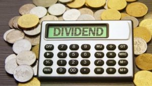 配当株: 「DIVIDEND」という言葉を投影する電卓は、金貨と銀貨の山の上にあります。