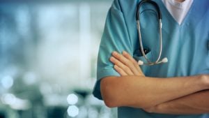 stay-at-home stocks Healthcare professional in green scrubs standing with arms crossed.