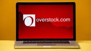 Image of overstock.com (OSTK) logo on a laptop with a plain yellow background. retail stocks