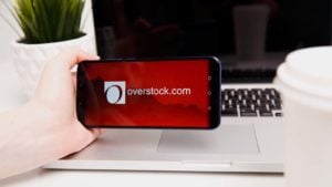 a hand holding an iPhone displaying the Overstock.com logo