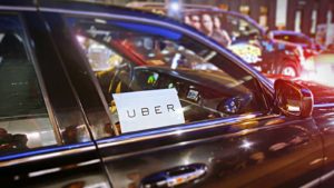 A photo of an Uber placard in the window of a car on a city street.