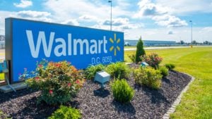 A photo of a Walmart sign in landscaping against a blue sky and a lawn.