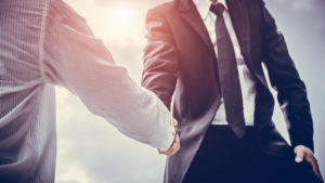 Two business men shaking hands in a sunny setting representing TLMD Stock.